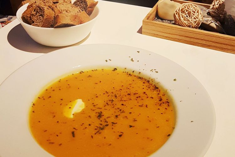 Ein Teller mit Kürbissuppe, im Hintergrund steht eine Schale mit Brot