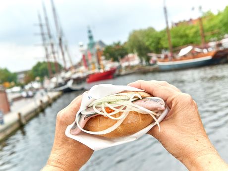 Eine Person hält ein Matjesbrötchen am Hafen von Emden
