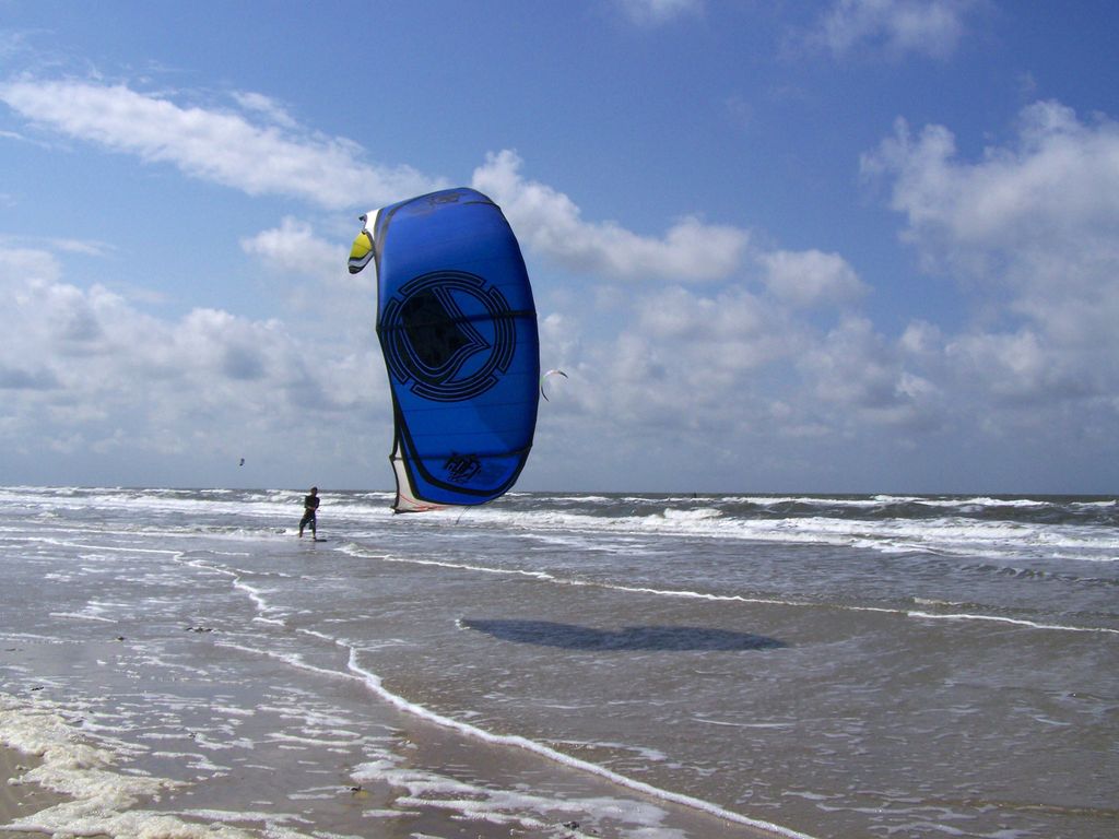 Ein Kitesurfer steht im Wasser und lenkt seinen blauen Kite