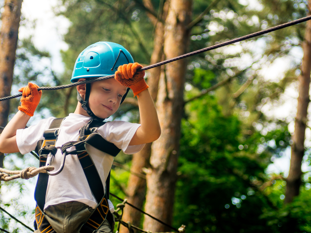 Junge mit Kletterausrüstung hangelt sich von Baum zu Baum