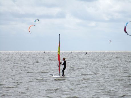 Eine Kitesurferin und Windsurfer im Hintergrund im Wasser bei Dornumersiel