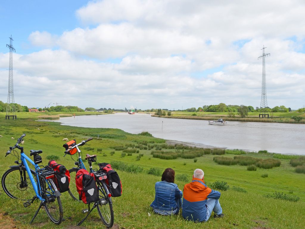 Urlauber sitzen auf dem Deich und schauen auf dem Fluss Jümme, Südliches Ostfriesland. 