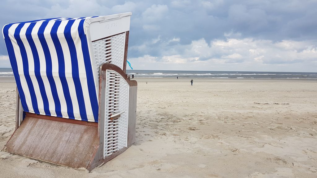 Detailblick auf einen blau-weiß-gestreiften Strandkorb im Sand an Strand von Norderney