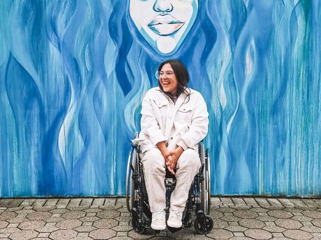 Das Foto zeigt die Bloggerin Kim von Wheeliewanderlust in ihrem Rolli vor einer bunt bemalten Wand