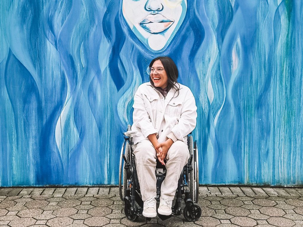 Das Foto zeigt die Bloggerin Kim von Wheeliewanderlust in ihrem Rolli vor einer bunten Wand